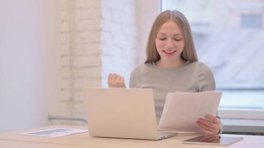 Creative Young Woman Celebrating while Doing Paperwork on Laptop