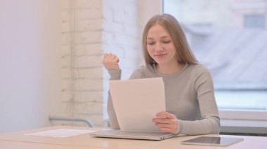 Creative Young Woman Celebrating while Reading Documents at Work