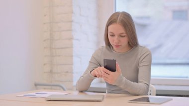 Creative Young Woman Browsing Internet on Smartphone at Work
