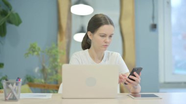 Young Woman using Phone and Laptop for Work