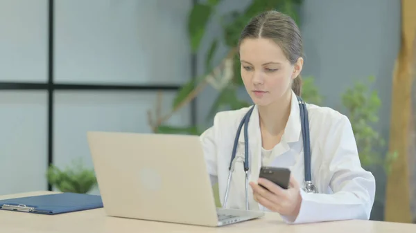 Νεαρή Γυναίκα Γιατρός Χρησιμοποιώντας Smartphone Κατά Χρήση Laptop — Φωτογραφία Αρχείου