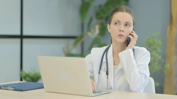 Νεαρή Γυναίκα Γιατρός Μιλώντας Στο Τηλέφωνο Ενώ Χρησιμοποιείτε Laptop — Φωτογραφία Αρχείου