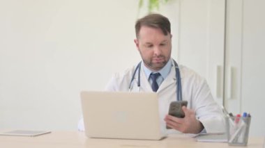 Genç Doktor Laptop ve Smartphone üzerinde çalışıyor.
