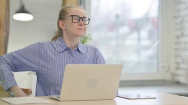 Sırt ağrısı olan genç bir kadın dizüstü bilgisayarda çalışıyor.