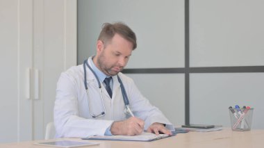 Genç Doktor evraklar üzerinde çalışıyor, evrak işleriyle uğraşıyor.