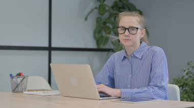 Dizüstü bilgisayarda çalışan genç kadın kameraya doğru bakıyor.