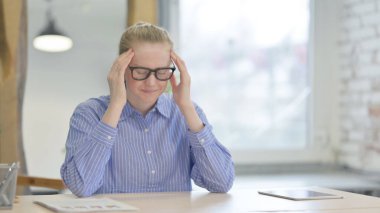 Yorgun genç kadın iş yerinde baş ağrısı çekiyor.