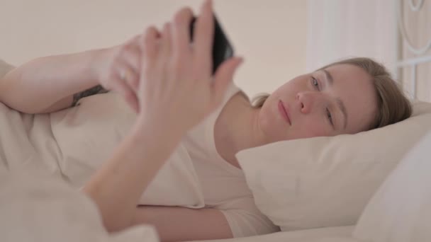 ベッドの中で携帯電話で話している若い女性 — ストック動画