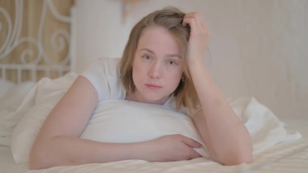 ベッドで肘に座りながらカメラを見ているシリアス若い女性 — ストック動画