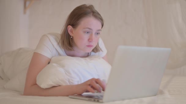 严肃的年轻女人躺在床上趴在胃上 用笔记本电脑看着相机 — 图库视频影像