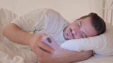 Yatakta telefon kullanan genç adamın yan görüntüsü