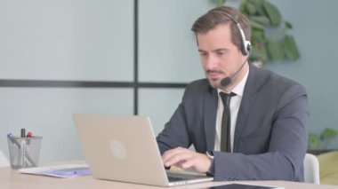 Kulaklıklı genç adam laptopta çalışıyor.