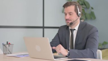 Kulaklıklı genç adam çağrı merkezinde müşterilerle konuşuyor.