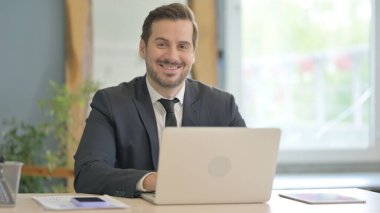 Bilgisayarda çalışırken kameraya gülümseyen iş adamı