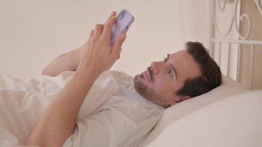 Yatakta telefon kullanan genç adamın yan görüntüsü