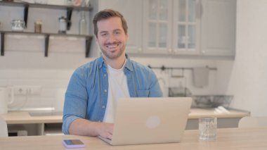 Bilgisayarda çalışırken kameraya gülümseyen genç adam