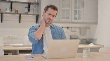 Boyun ağrısı olan genç adam dizüstü bilgisayarla çalışıyor.