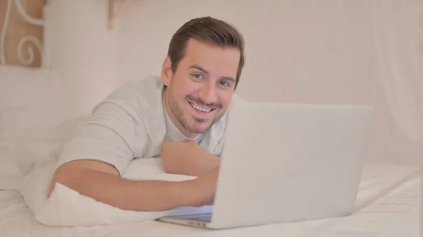 Smiling Young Man Looking Camera While Using Laptop Lying Stomach — Stok Foto