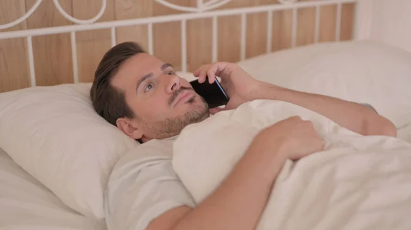 躺在床上的性情烦躁的男人在电话里辩论 — 图库照片