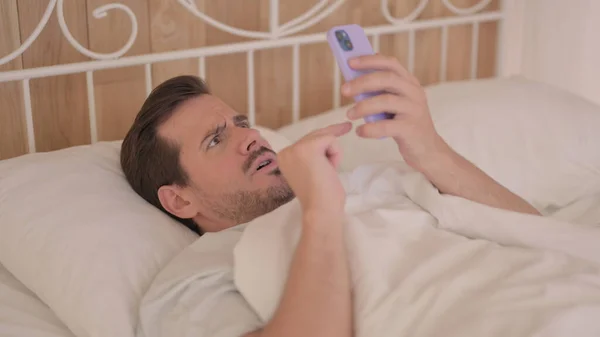 Unge Man Chockad Förlust Telefon När Ligger Sängen — Stockfoto