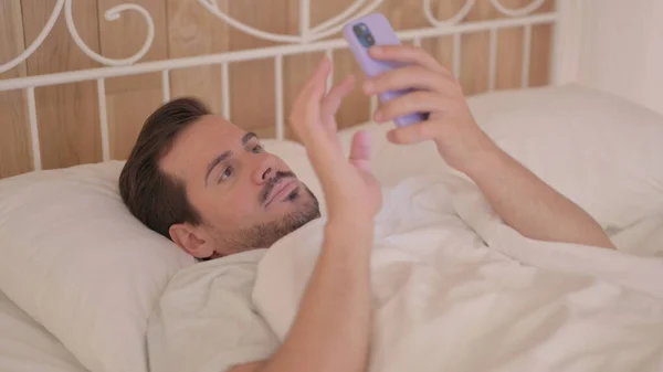 躺在床上用手机的年轻人 — 图库照片