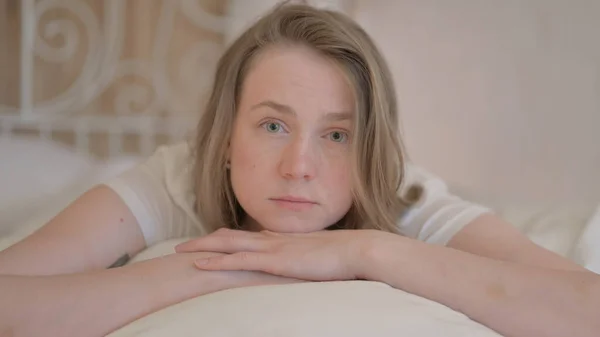 Poważna Młoda Kobieta Leży Łóżku Brzuchu Patrząc Aparacie — Zdjęcie stockowe