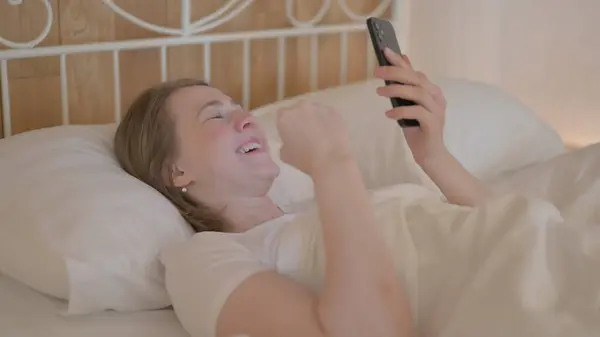Ung Kvinna Firar Framgång Smartphone Medan Liggandes Sängen — Stockfoto
