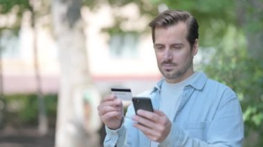 Bir bankta otururken internetten alışveriş yapan heyecanlı genç adam.