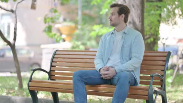 Entspannter Junger Mann Sitzt Draußen Auf Bank — Stockvideo