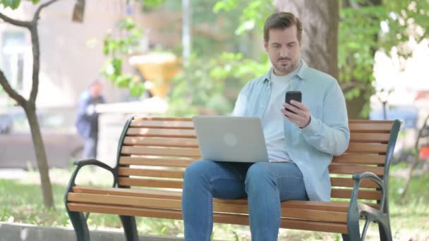 Mladý Muž Pomocí Smartphonu Notebooku Při Sezení Venku — Stock video