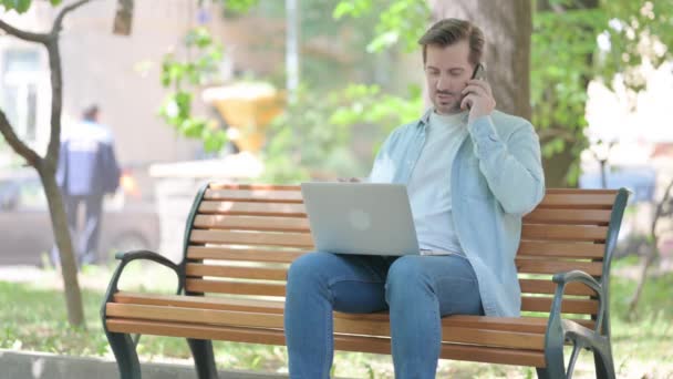 Mladý Muž Mluví Telefonu Při Používání Notebooku Venkovní — Stock video