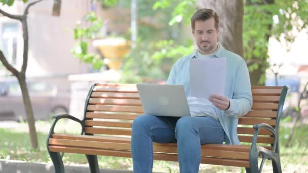 Молодой Человек Сидящий Свежем Воздухе Осматривающий Документы Ноутбук — стоковое видео