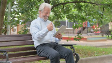 Bir bankta otururken Tablette Başarı Kutlaması Yapan Yaşlı Yaşlı Adam