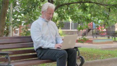 Laptop kullanan yaşlı bir adam öksürüyor.