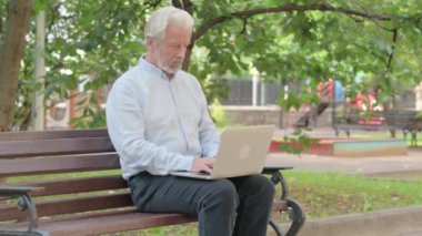 Üst düzey yaşlı adam laptopta çalışırken kameraya bakıyor.