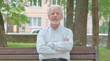 Dışarıda oturan yaşlı adam kameraya gülümsüyor.
