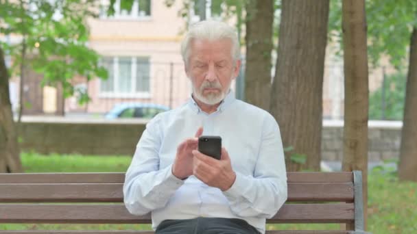 Älterer Mann Jubelt Online Auf Smartphone Während Auf Bank Sitzt — Stockvideo