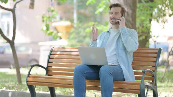 Angry Young Man Talking Phone While Using Laptop Outdoor — Stock Photo, Image