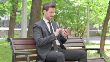 Genç İşadamı bir bankta otururken akıllı telefon kullanıyor.