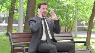 Genç İşadamı dışarıda bankta otururken telefonda tartışıyor.