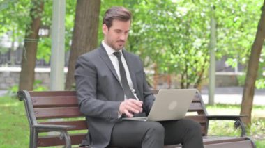 Genç İşadamı dizüstü bilgisayarla çalıştıktan sonra Bench 'i açık havada bırakıyor.