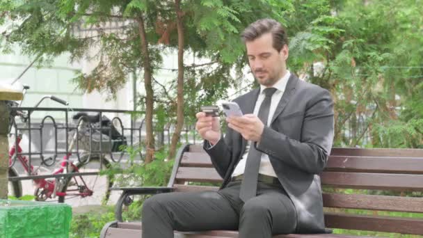 Geschäftsmann Mittleren Alters Macht Online Einkäufe Telefon Während Draußen Sitzt — Stockvideo