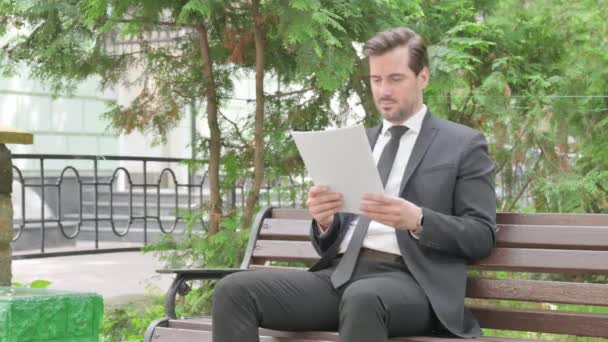 Geschäftsmann Mittleren Alters Liest Dokumente Während Draußen Sitzt — Stockvideo