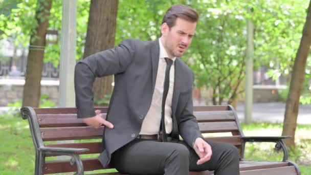 背中の痛みと屋外に座っている若いビジネスマン — ストック動画