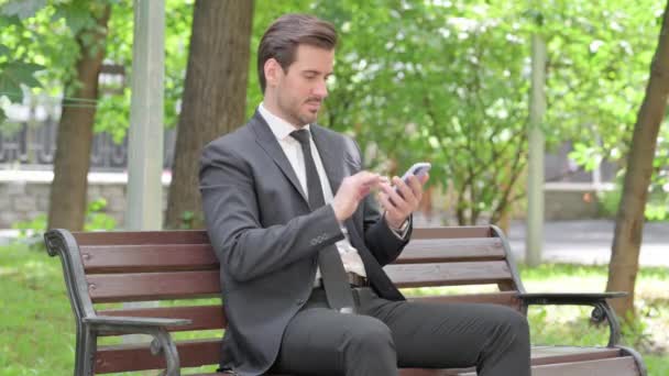 Pengusaha Muda Menggunakan Smartphone Ketika Duduk Outdoor Pada Bench — Stok Video