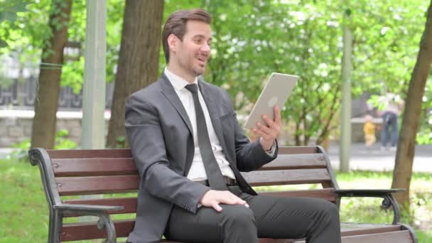 ベンチに屋外に座っている間 タブレットでビデオチャットをする若いビジネスマン — ストック動画
