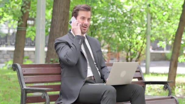 Businessman Muda Berbicara Telepon Dan Menggunakan Laptop Outdoor — Stok Video