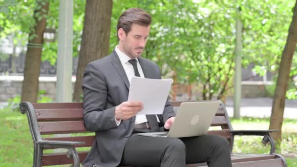 ドキュメントとラップトップ屋外で働く若いビジネスマン — ストック動画