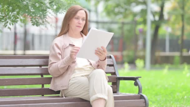 Seniorin Liest Dokumente Während Sie Draußen Sitzt — Stockvideo