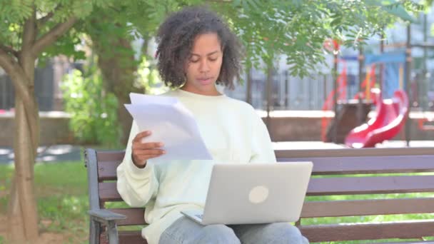 カジュアルなアフリカの女性は契約を読み 屋外でラップトップを使用しながら浮気を感じます — ストック動画